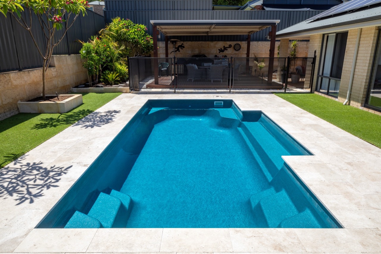 A rectangular fibreglass pool with built-in steps and bench seat beside a covered alfresco area in a landscaped Brisbane, QLD backyard
