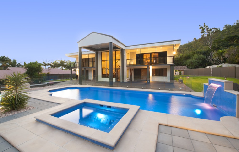A large fibreglass pool and matching clip-on spa with a feature water blade in a landscaped backyard at dusk